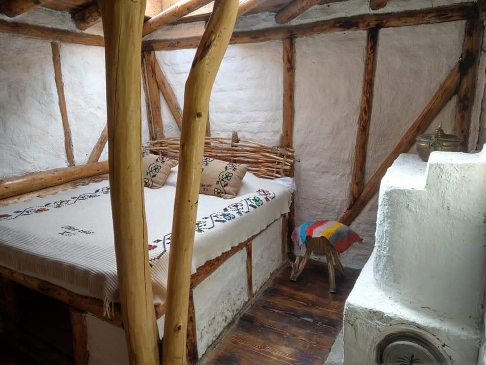 dormitor mic, cu pereti albi si barne de lemn, su un pat tradițional