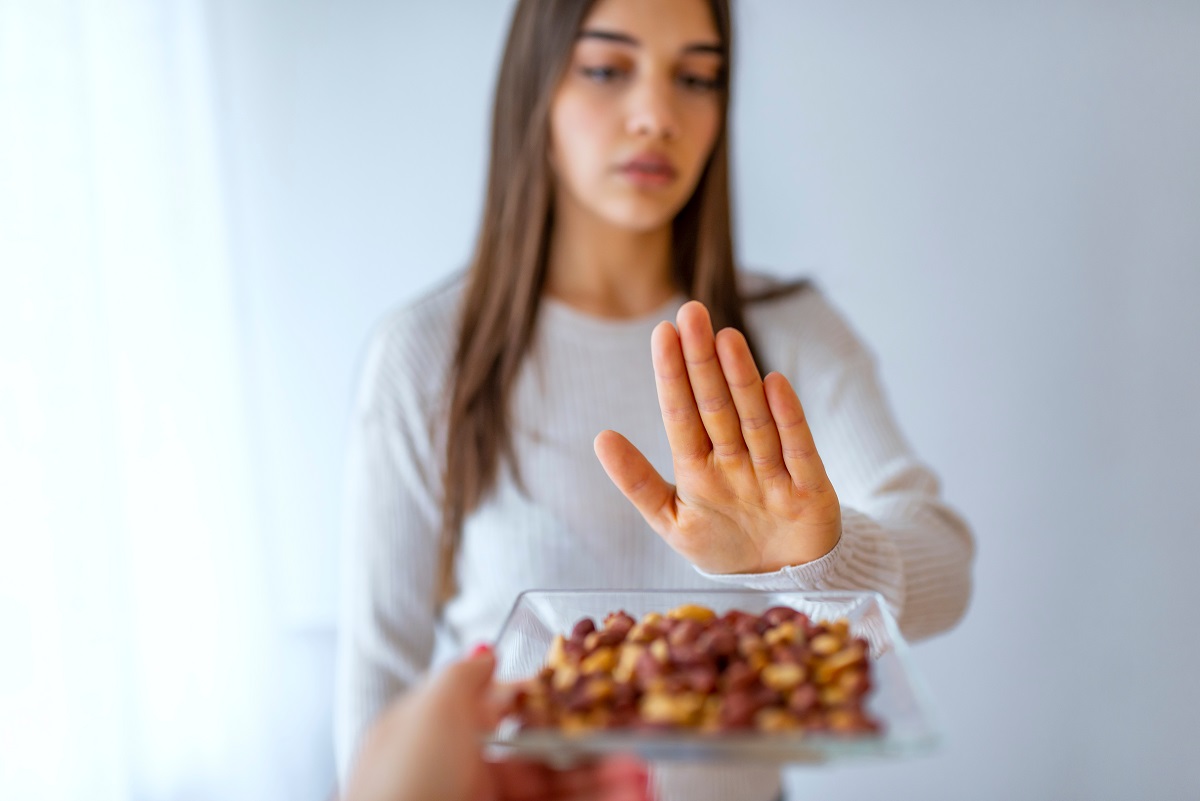 Fotografie concept pentru alergii alimentare la alune: femeie care intinde mana in semn de refuz catre o farfurie cu alune