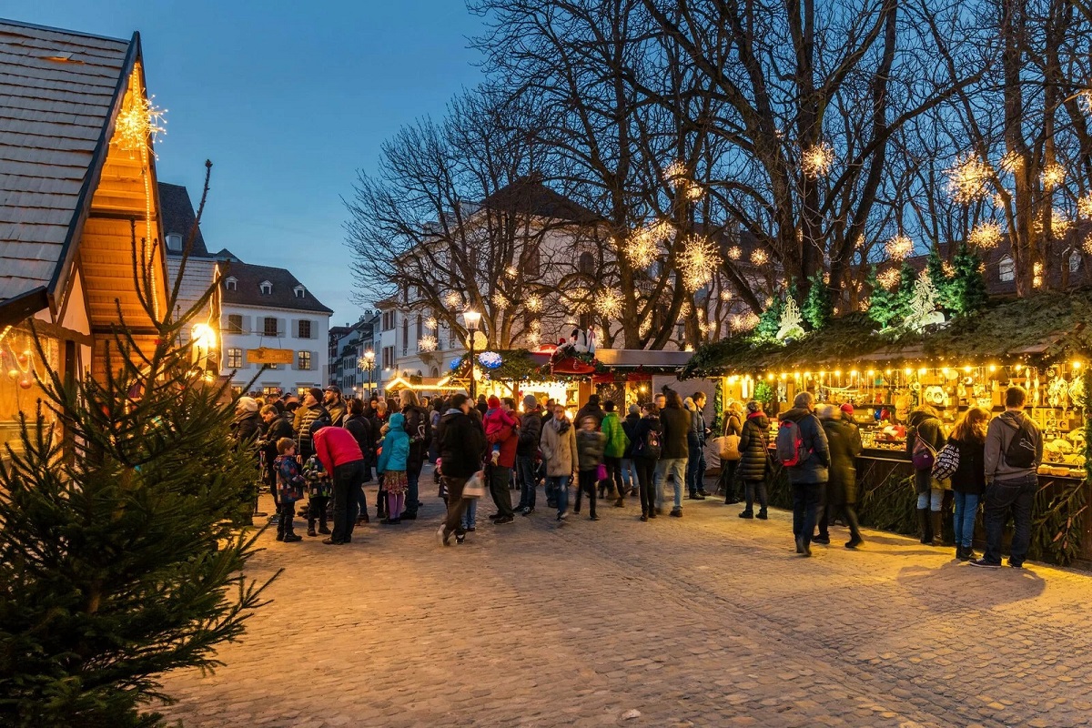 oamni care se plimba printre casutele cu produse traditionale latârgul de Crăciun din Basel, Elveția, cu o alee larga si decoratiuni luminoase de sarbatoare. unul dintre cele mai frumoase târguri de Crăciun din Europa
