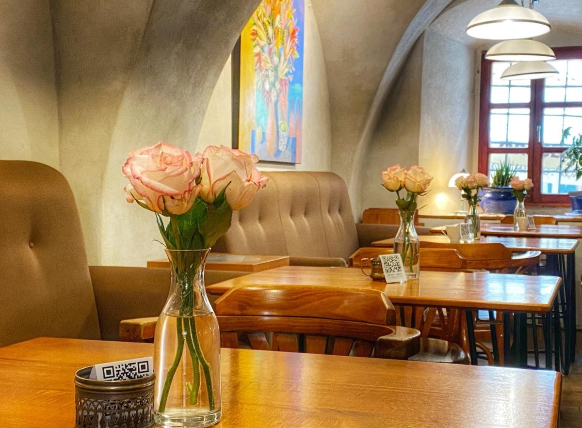 close up cu o masa din restaurantul Bistro De l'arte, cu o vaza cu trandafir roz, iar in fundal canapele si pereti boltiti, cu tablouri, unu din restaurantele din țară cu bucătărie românească modernă