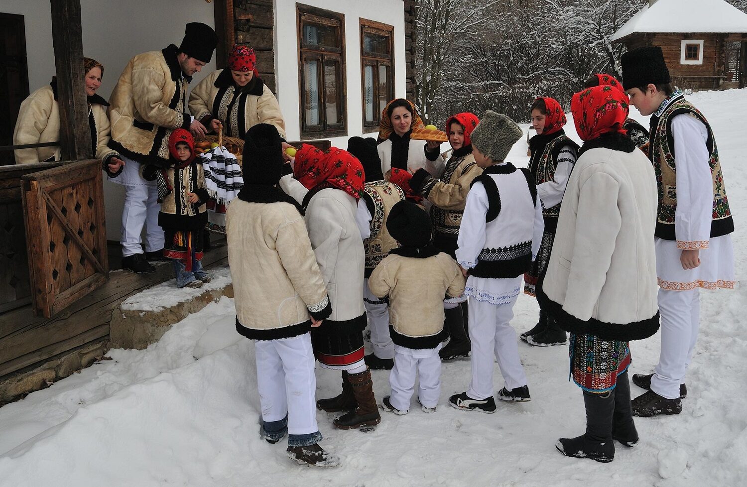 grup de colindători, copii, in costume traditional romanesti, care primesc covrigi de la gazedele adulte, imbracatae tot in costume nationale. Craciun în Bucovina. Crăciun autentic românesc 