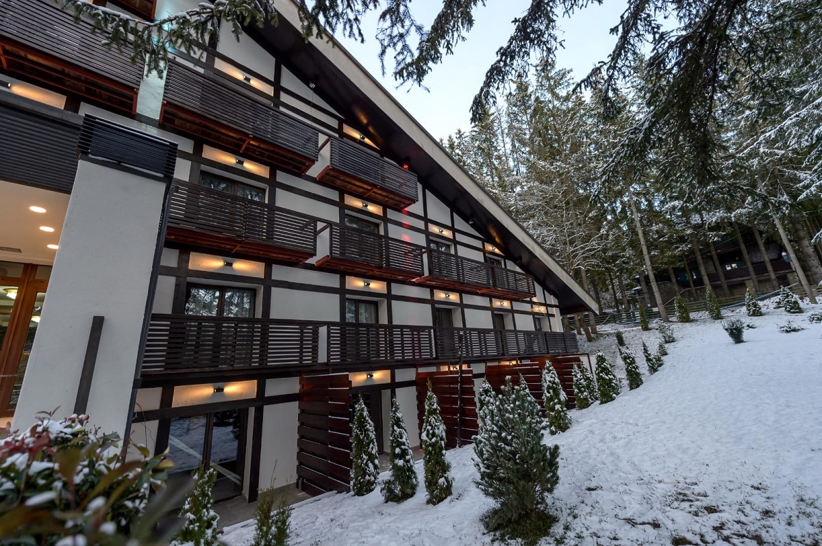 Hotel Elexus Predeal cu acoperis oblic, fotografiat iarna printre copacii plini de zapada, un loc und esă-ți faci Revelionul la munte la Predeal