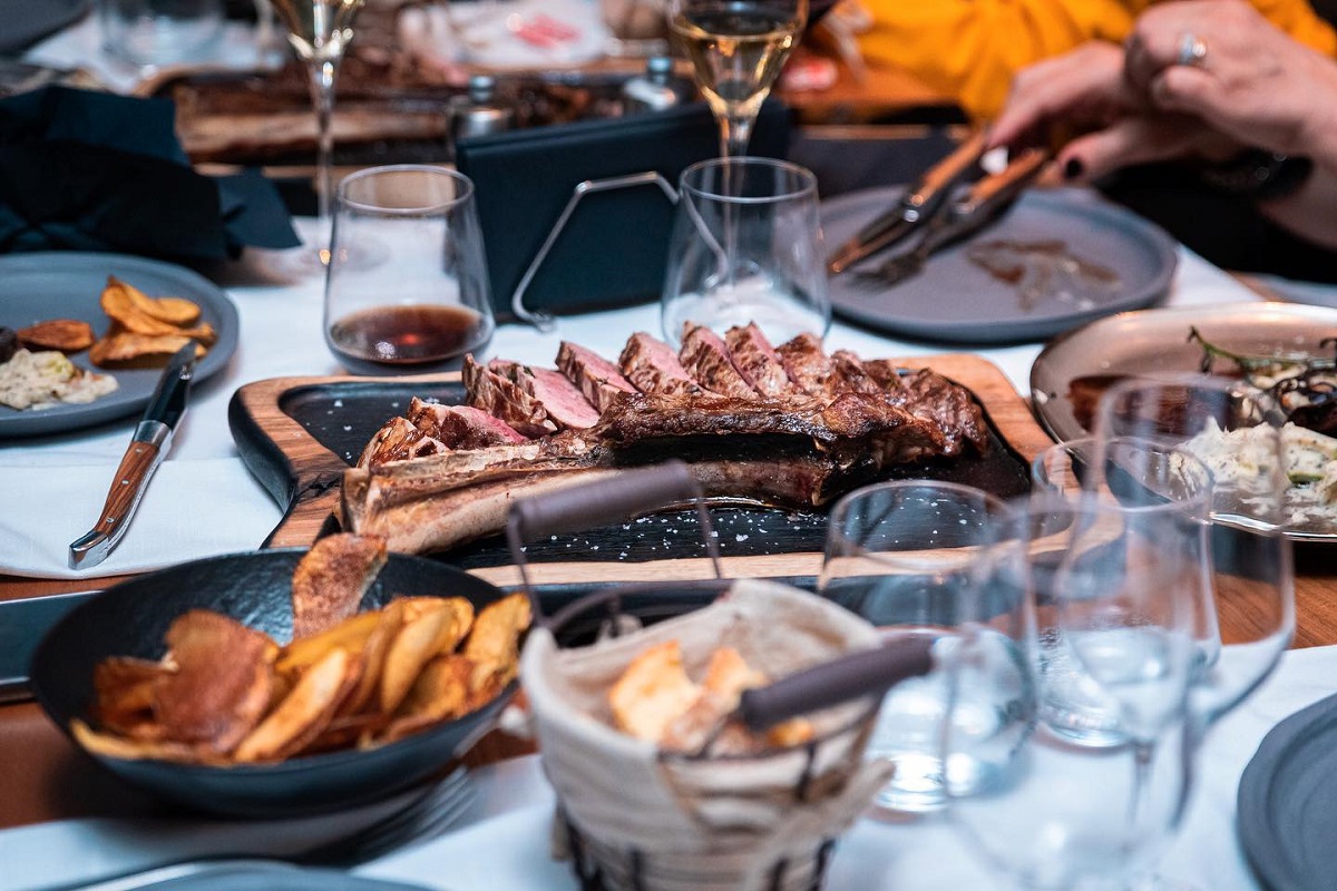 close up cu o masa la Ferma Baciu, cu pahare, farfurii si un platiou mare cu friptură tăiată felii, unde să mergi de 1 decembrie la restaurant