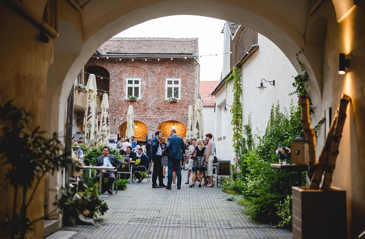 curtea restaurantului Jules Bistro, fotografiata prin dreptul unei arcade zidite, plina de oameni care iau masa. Unul dintre cele mai bune restaurante din Sibiu