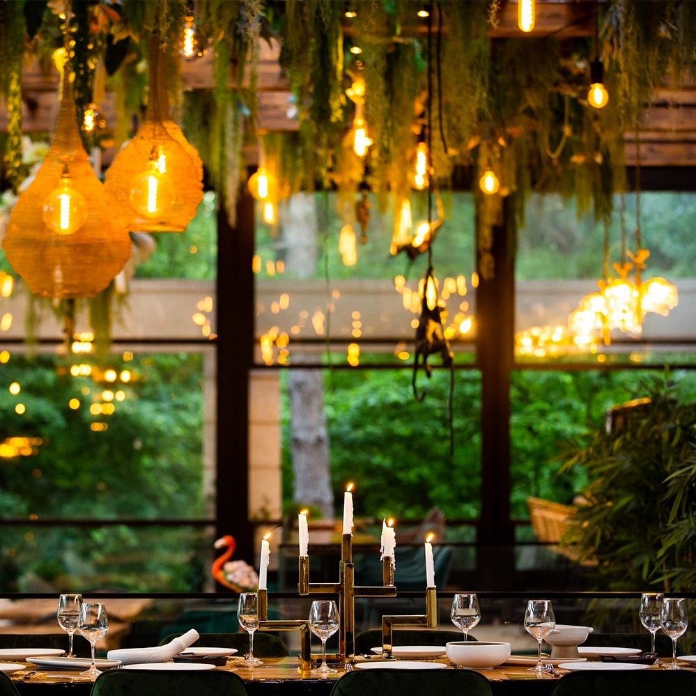 masa cu lumanari si deasupra decoratiuni din plante si corpuri de iluminat aprinse la restaurant Kong, potrivit pentru petrecerea de Crăciun a firmei