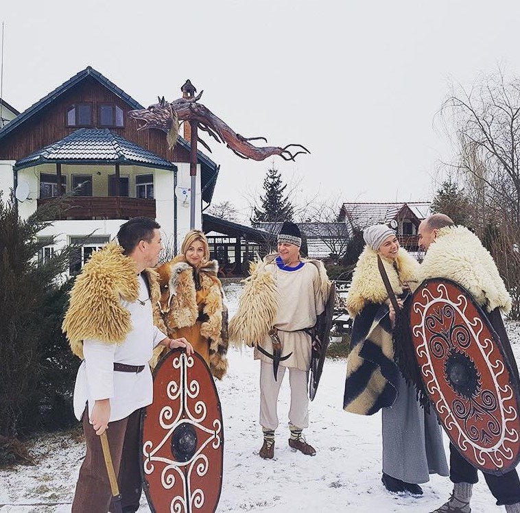 grup de oameni imbaracati in costume traditionale, ca niste daci, cu scuturi pictate in mana, iarna, cu zapada, iar in fundal pesniunea cotiso
