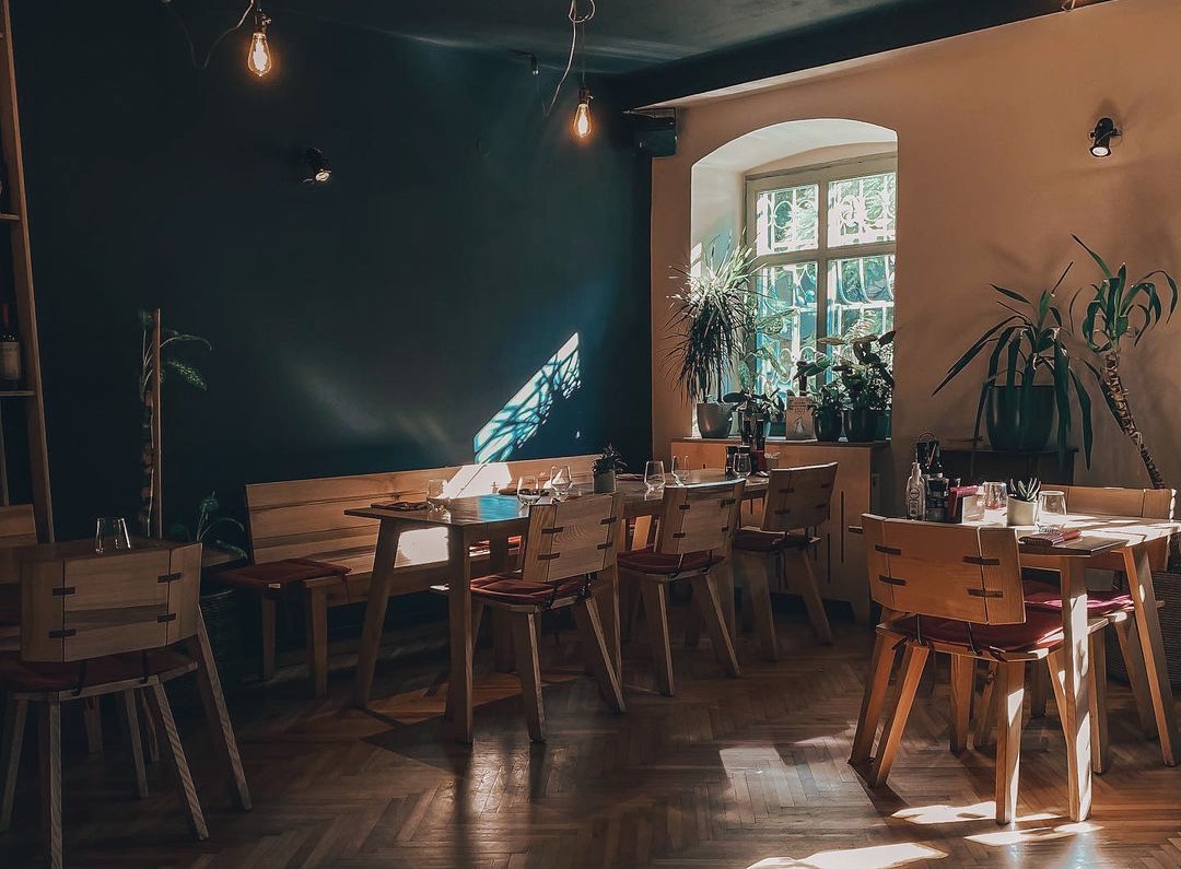 incapere fotografiata in semiumbra, cu un prete verde inchis, mese si plante ornamentale, la restaurant Hochmeister, unul dintre cele mai bune restaurante din Sibiu