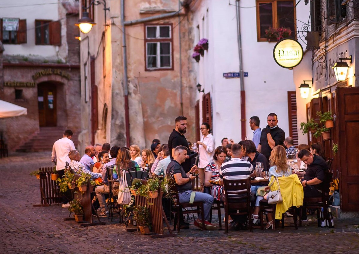 oameni care servesc masa afara, pe trotuar, in dreptul restaurantului Pasaj, unul dintre cele mai bune restaurante din Sibiu
