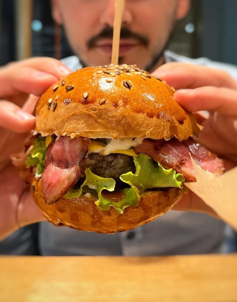 close up cu un burger tinut in maine de un barbat