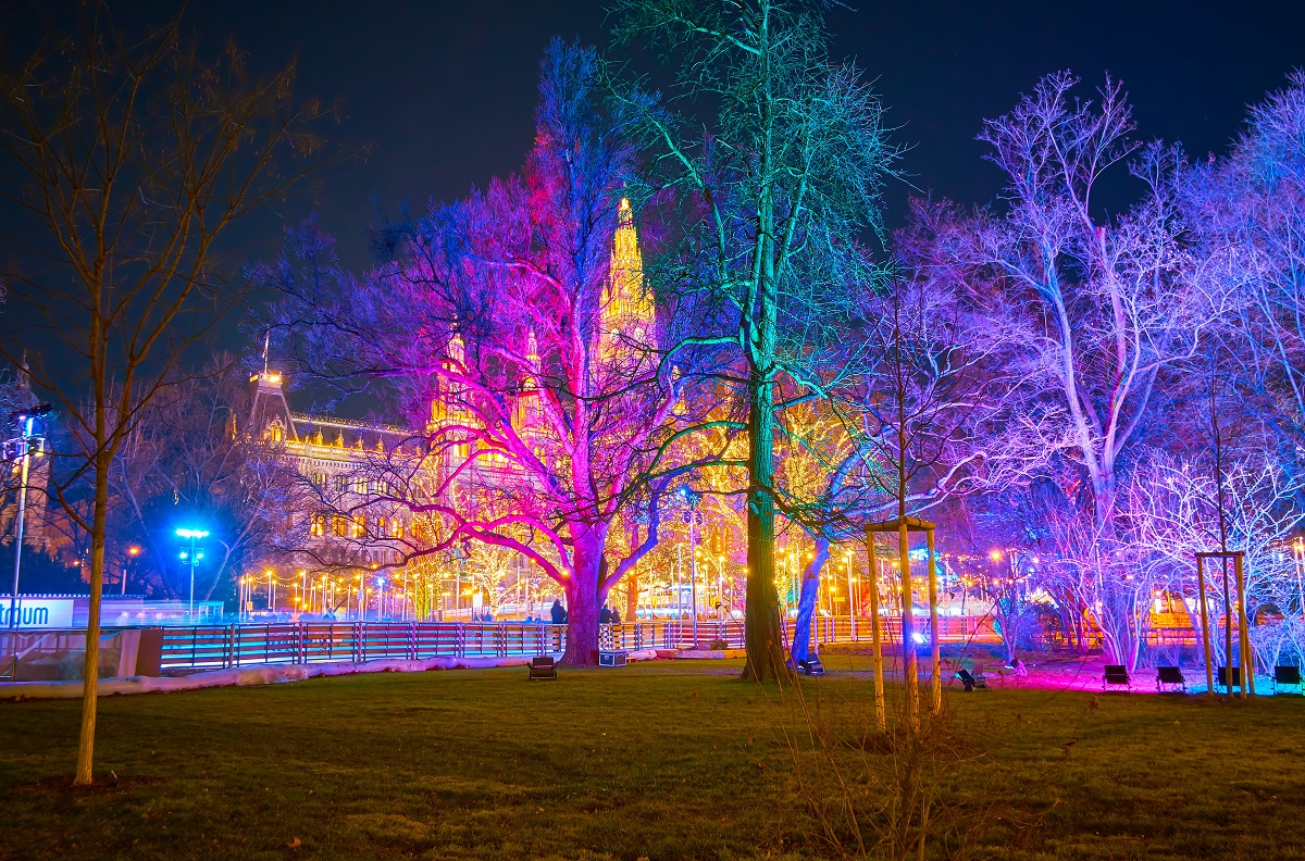 VIENNA, AUSTRIA - FEBRUARY 18, 2019: The view on illuminated Rathaus (Town Hall) and ice skating rink through the trees of Rathauspark in colorful evening lights, on February 18 in Vienna.