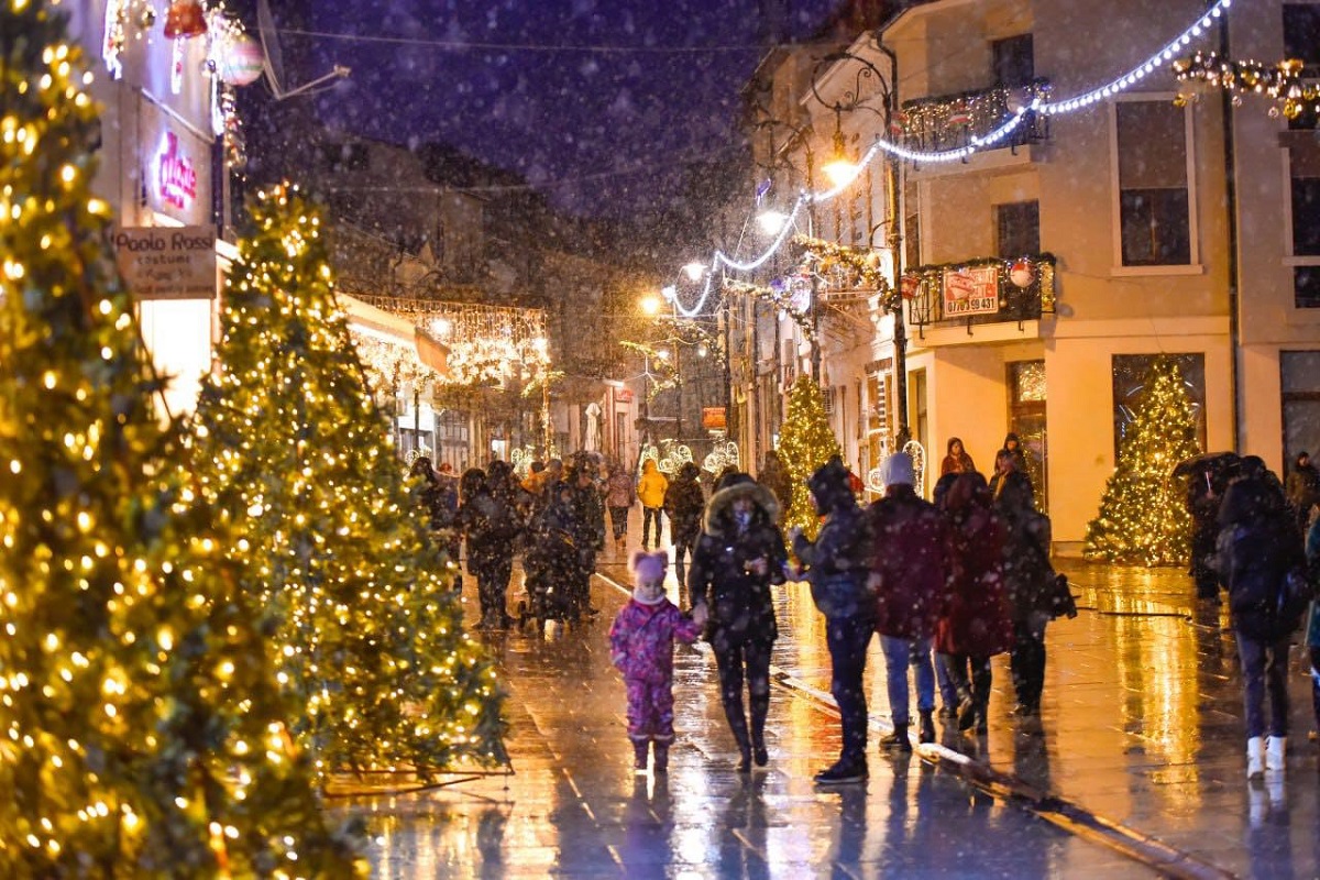 trecatori pe strazile impodobite, din Craiova, intr-o seara cu ninsoare