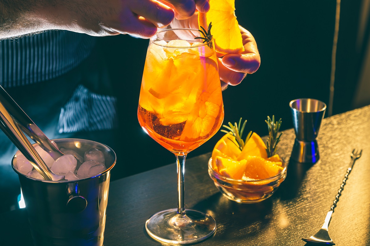 Bartender decorating Aperol spritz cocktail, adding a slice of orange onto a rim of a wineglass