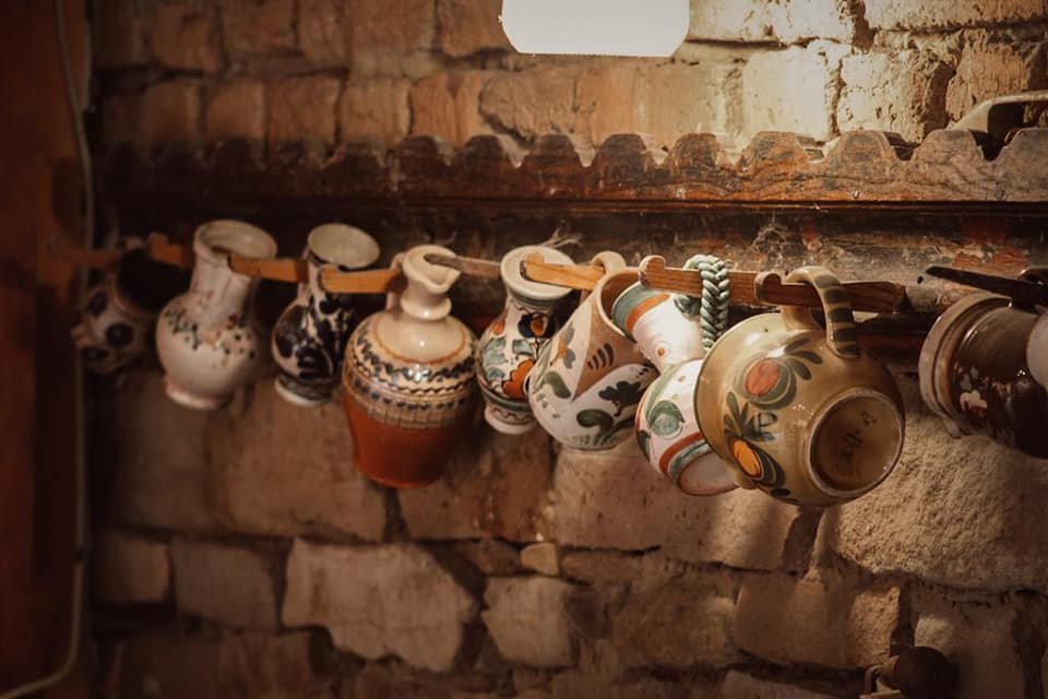vase din lut traditional romanesti, prinse in carlige pe un bat tinutuit de peretele din caramida