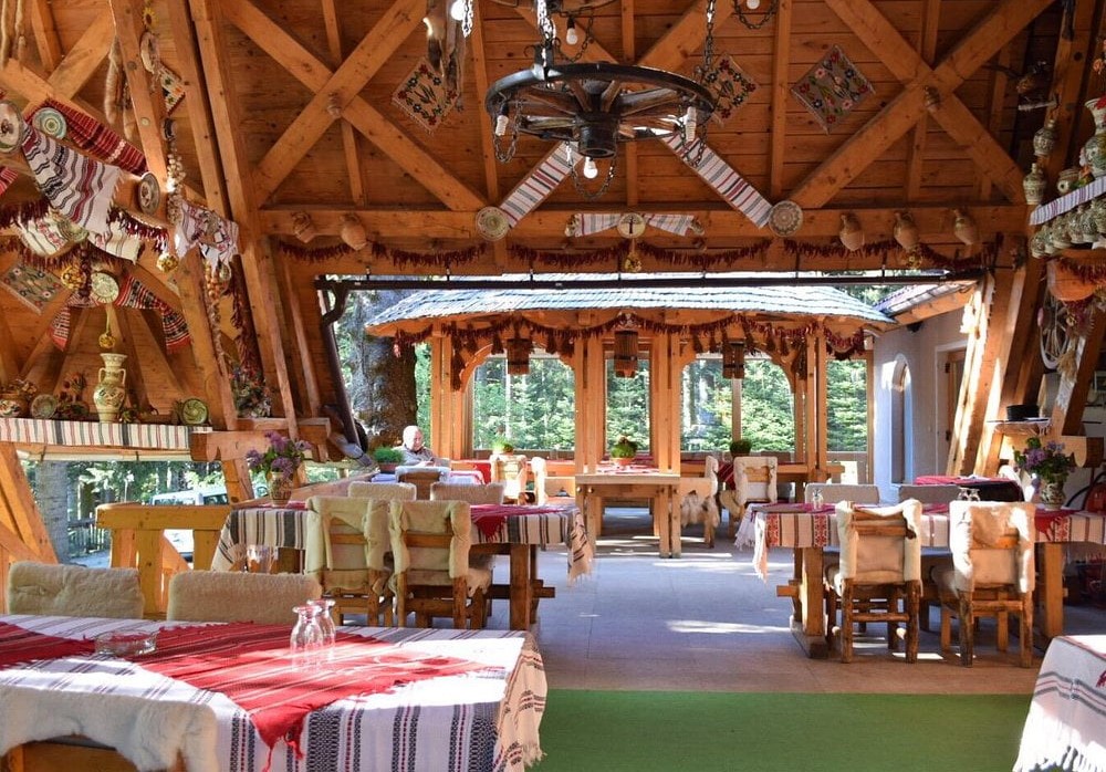 Restaurant Coliba Haiducilor, traditional romanesc, din lemn, cu tavan inalt si mese de lemn, iar in fundal ferestre mari prin care se vede afară - und emâncăm în Poiana Brașov
