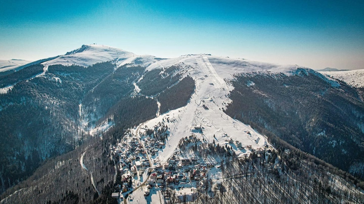varful muntelui Vâlcan din Straja, acoperit de zapada, cu partii de schi amenajate, si stațiunea Straja fotografiata din departare, de sus, una din stațiuni de schi populare din România