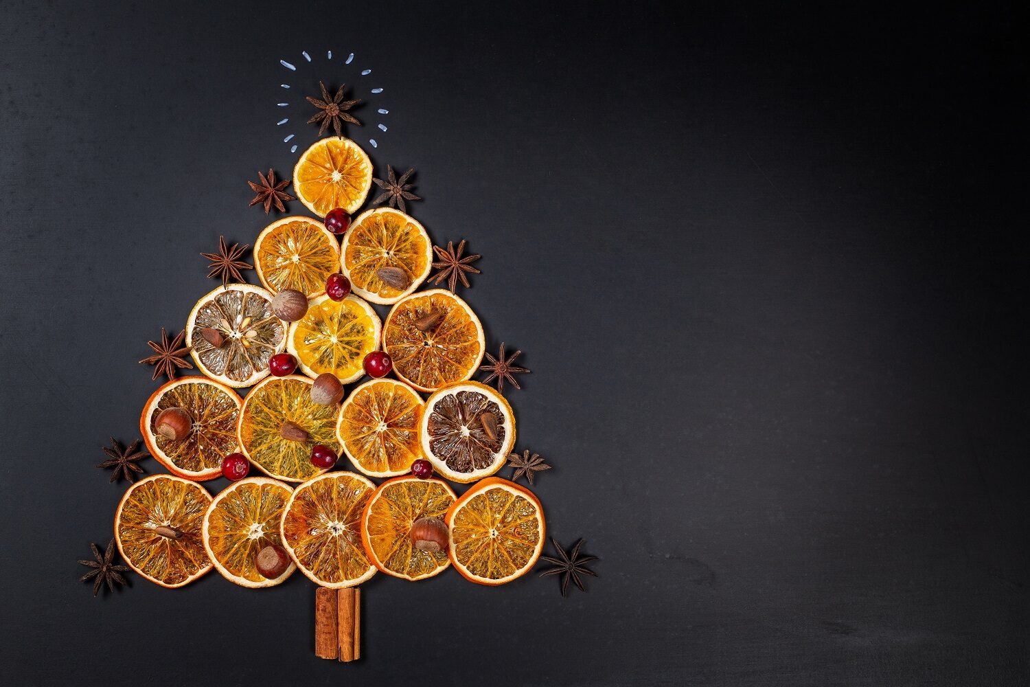 Pom de Crăciun realizat din felii de portocala uscate, betisoare de scortisoara si stea de anason in varf , fotografiat de fundal negru - imagine concept pentru condimente și mirodenii de Crăciun