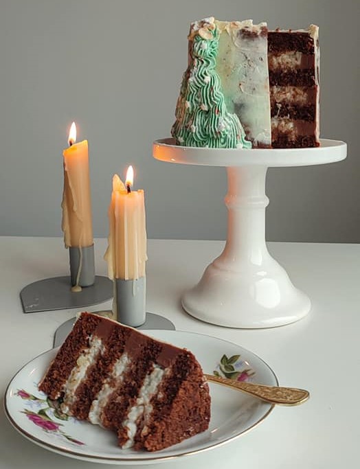 tort gingerbread asezat pe suport alb de tort, alaturi de 2 lumanari aprinse si o felie de tort asezata pe farfurie alba de la Luna Magică București