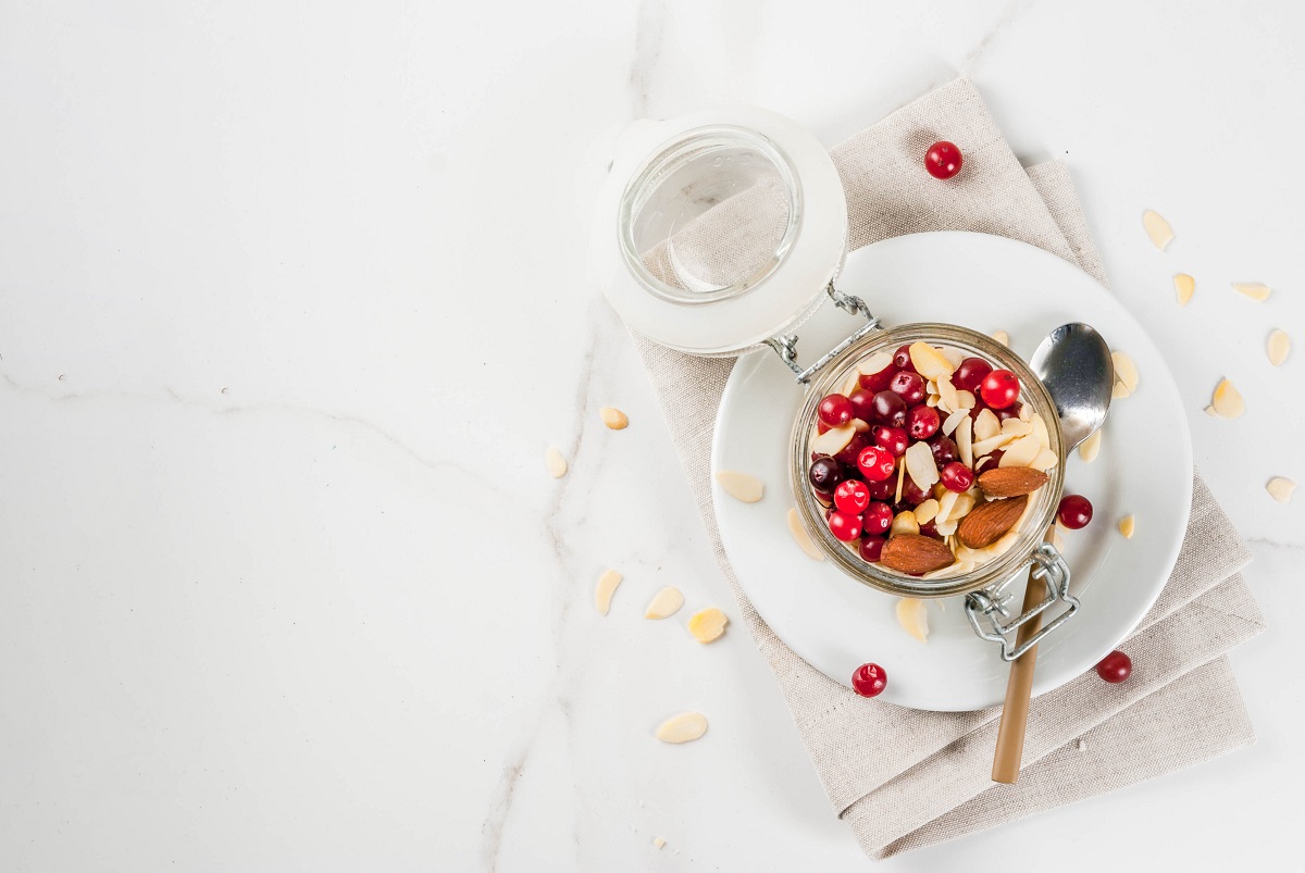 Recipe for a healthy winter breakfast, ideas for Christmas morning. Overnight oatmeal with almonds, cranberries, sugar. On a white marble table. copy space top view