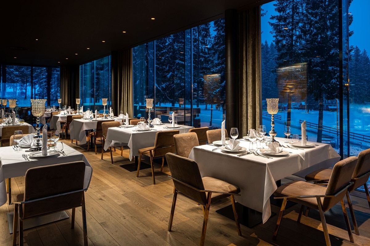 Restaurant Altitude din Poiana Brasov, luxos, elegant, cu un sir de mese in dreptul peretelui din ferestre mari, prin care se vede peisajul seara, nins - und emâncăm la restaurant îmn Poiana Brașov 