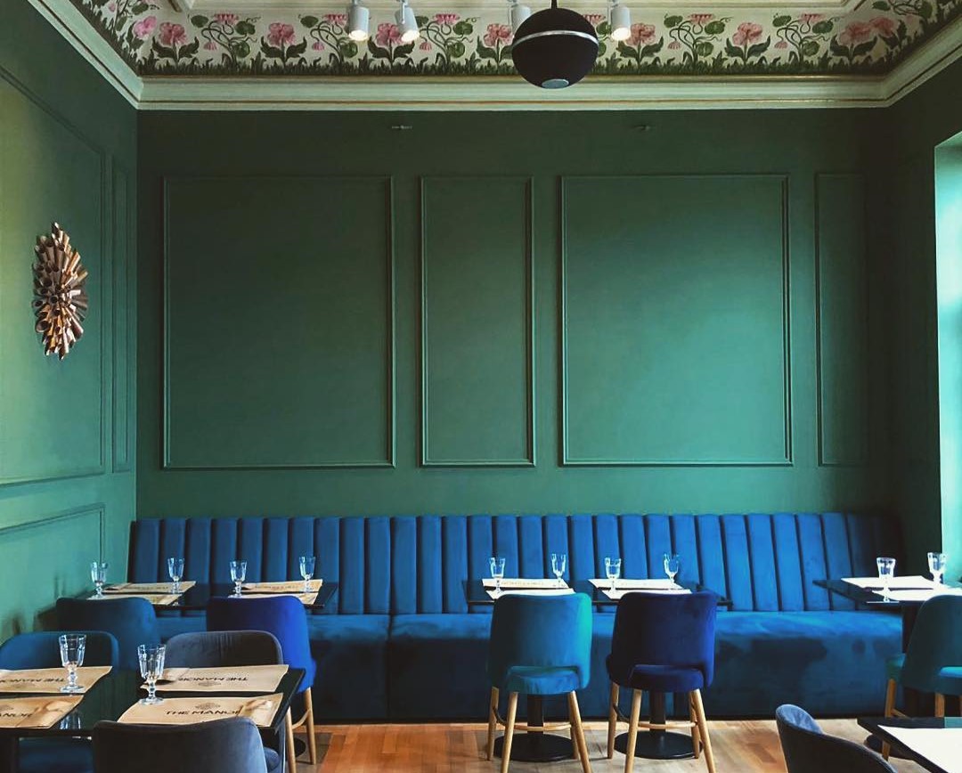 interiorul restaurantului The Manor din Craiova, cu scaune si canapele din catifea albastra, si peretii verde inchis, cu stucaturi 