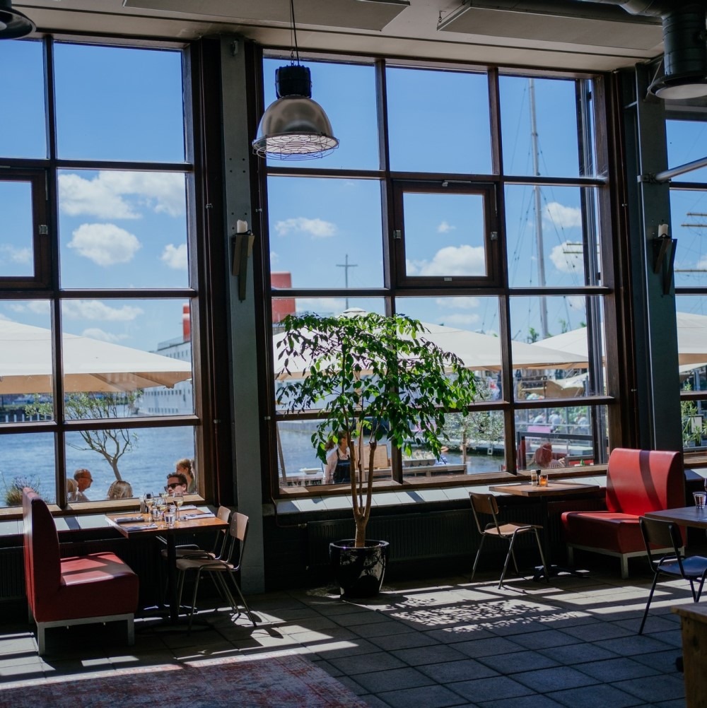 sala de mese cu ferestre mari cat peretele si in dreptul lor canapele cu mese la restaurant Ij-Kantine din Amsterdam