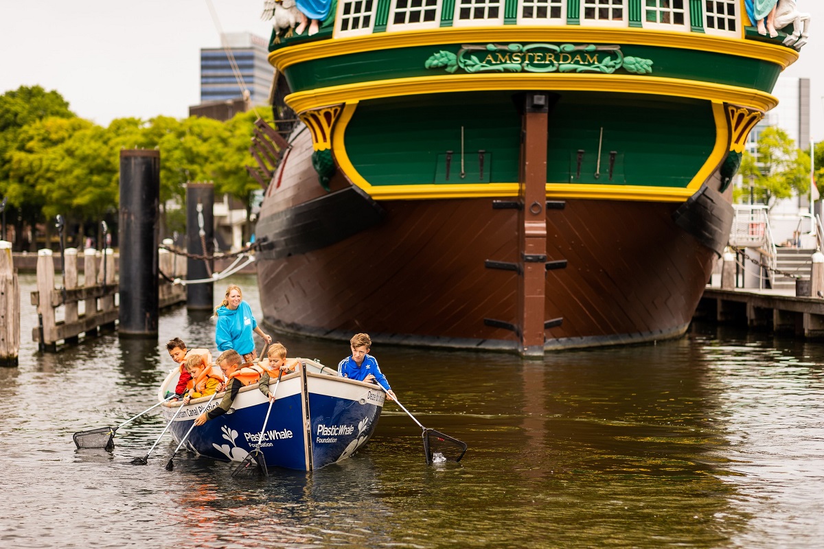 copii care vaslesc intr-o barca, in fata unui vapor mai mare, la Scheepvaartmuseum Amsterdam