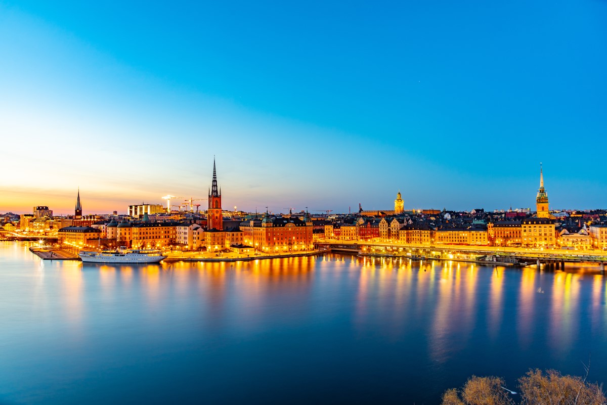 Stockholm fotografiat de la distanta, seara, cu toate luminile ora;ului aprinse si cu apa albastra in prim plan