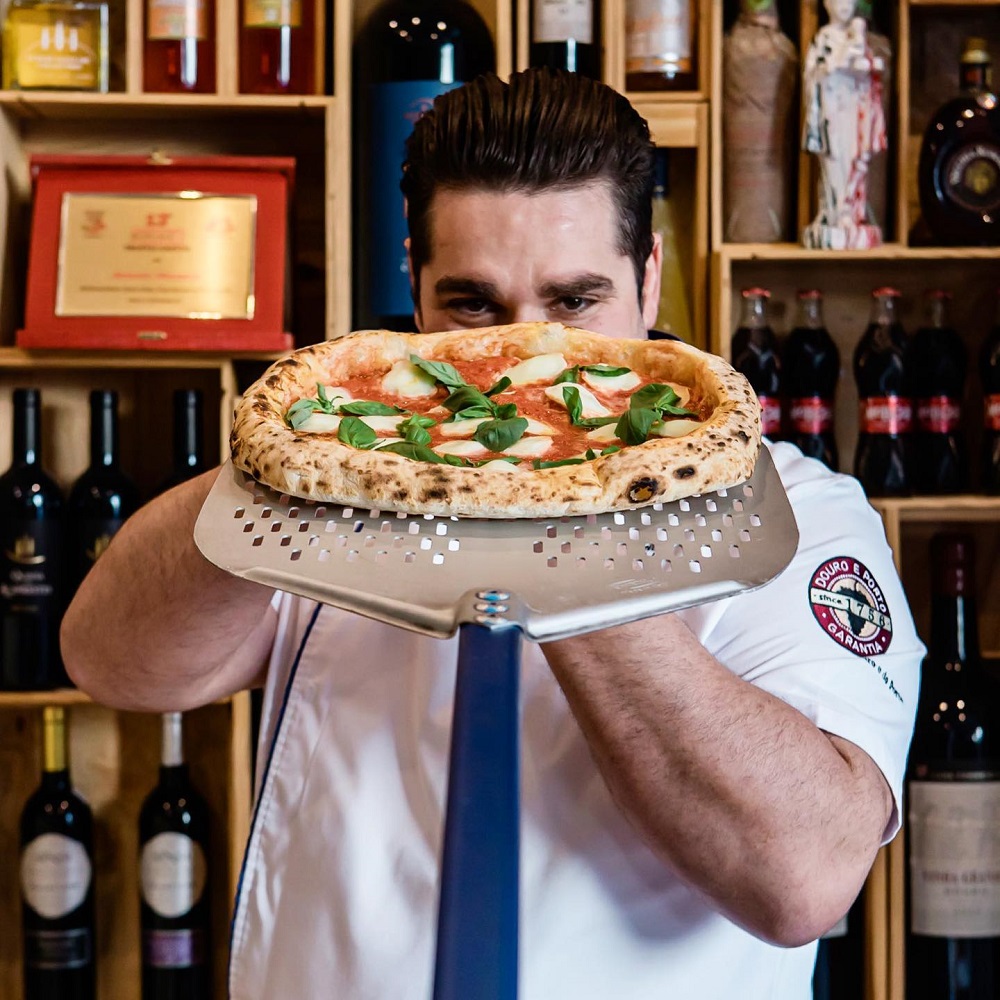 Antonio Mezzero la pizzeria din Porto, tinand in maini o pizza ca si cum o serveste cuiva