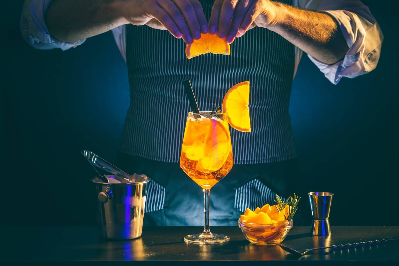 Bartender decorating Aperol spritz cocktail, adding a slice of orange on a wineglass filled with ice - imagine reprezentativă pentru ce se bea în 2023