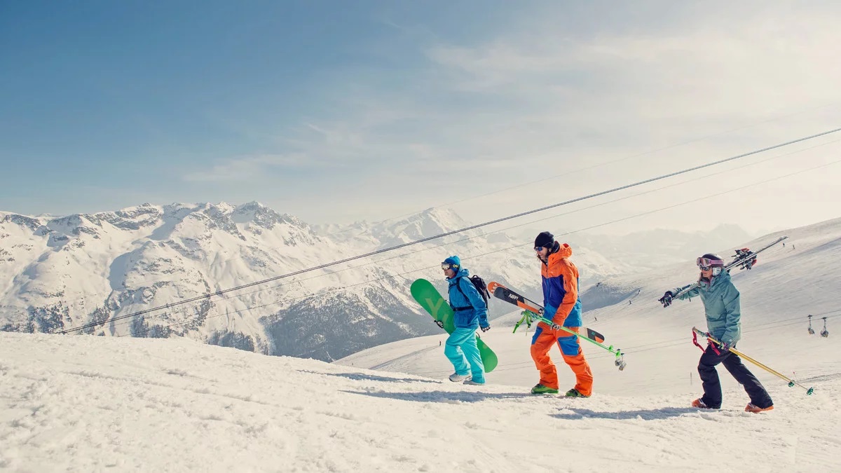 3 tineri in costum de schi, care cara placile de snowboard pe partie in ST. Moritz