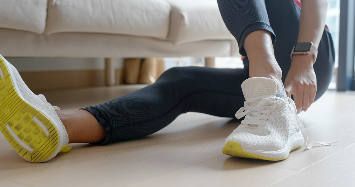 close up cu picioarele unei femei imbracata in colanti negri care se incalta cu o pereche de adidasi - imagine sugestiva pentru jogging - obiceiurile sănătoase