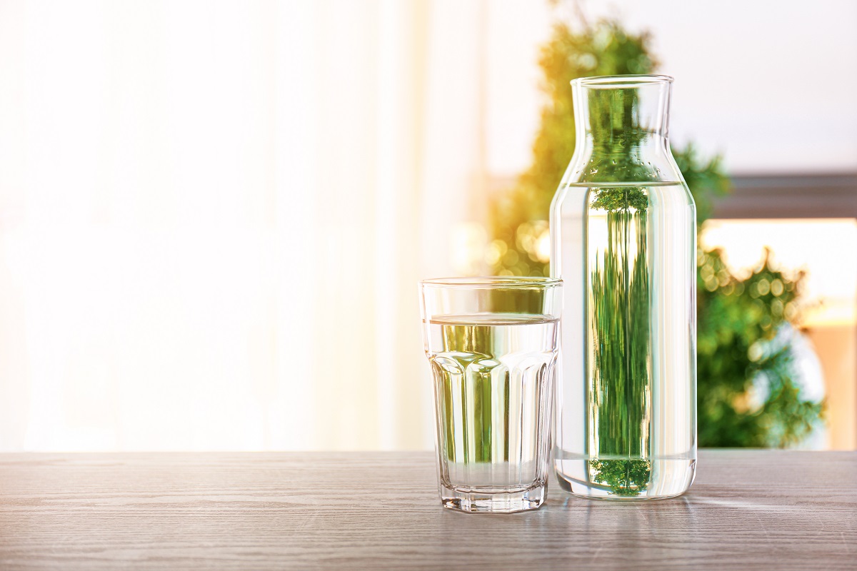 sticla si pahar cu apa, asezata pe o masa - imagine pentru hidratarea corecta- cum revii la obiceiurile sănătoase