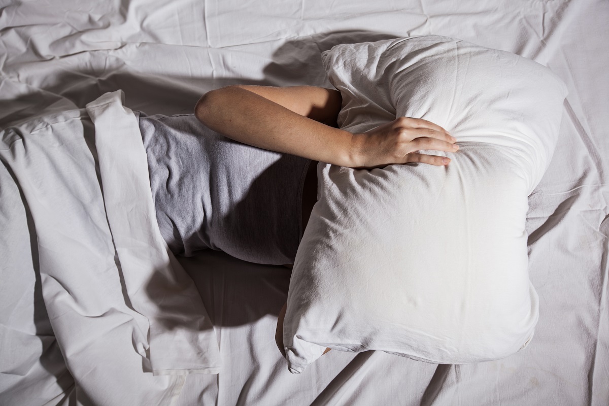Female with insomnia cover her face with pillow in bed.
