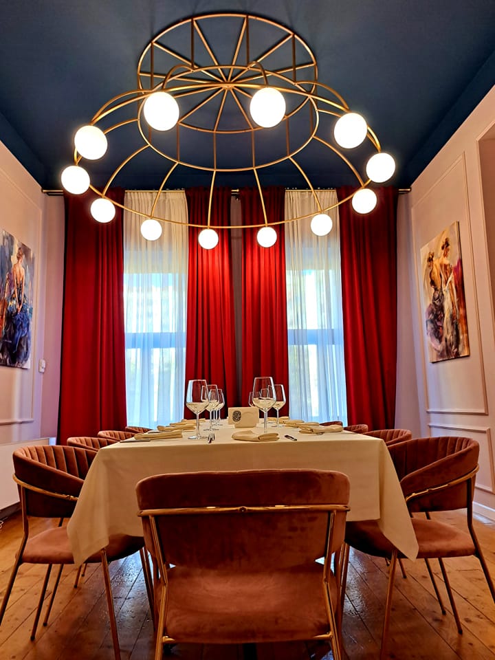 candelabru mare, rotund, desupra unei mese, in fata unei ferestre cu draperii din catifea rosie la Trai Restaurant, unul din restaurante bune din Iași