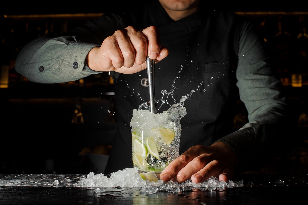 Professional bartender prepare a fresh lime cocktail in the glass with an ice at the steel barstand - imagine reprezentativa pentru ce se bea în 2023