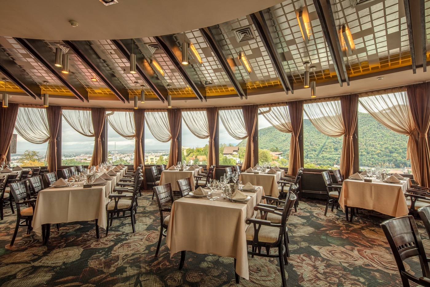 Restaurant Belvedere din Brasov, cu salon circular, cu ferestre mari prin care se vede muntele și orașul, amenajat elegant. Unul din restaurante skybar & rooftops