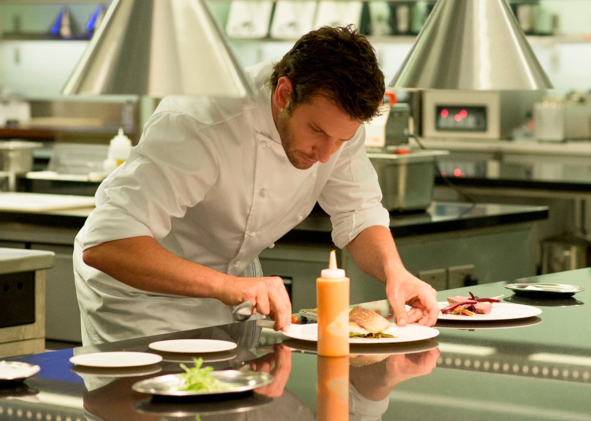 Bradley Cooper în costum de bucatar, aranjeaza o farfurie in filmul Burnt - unul din filme pentru foodies