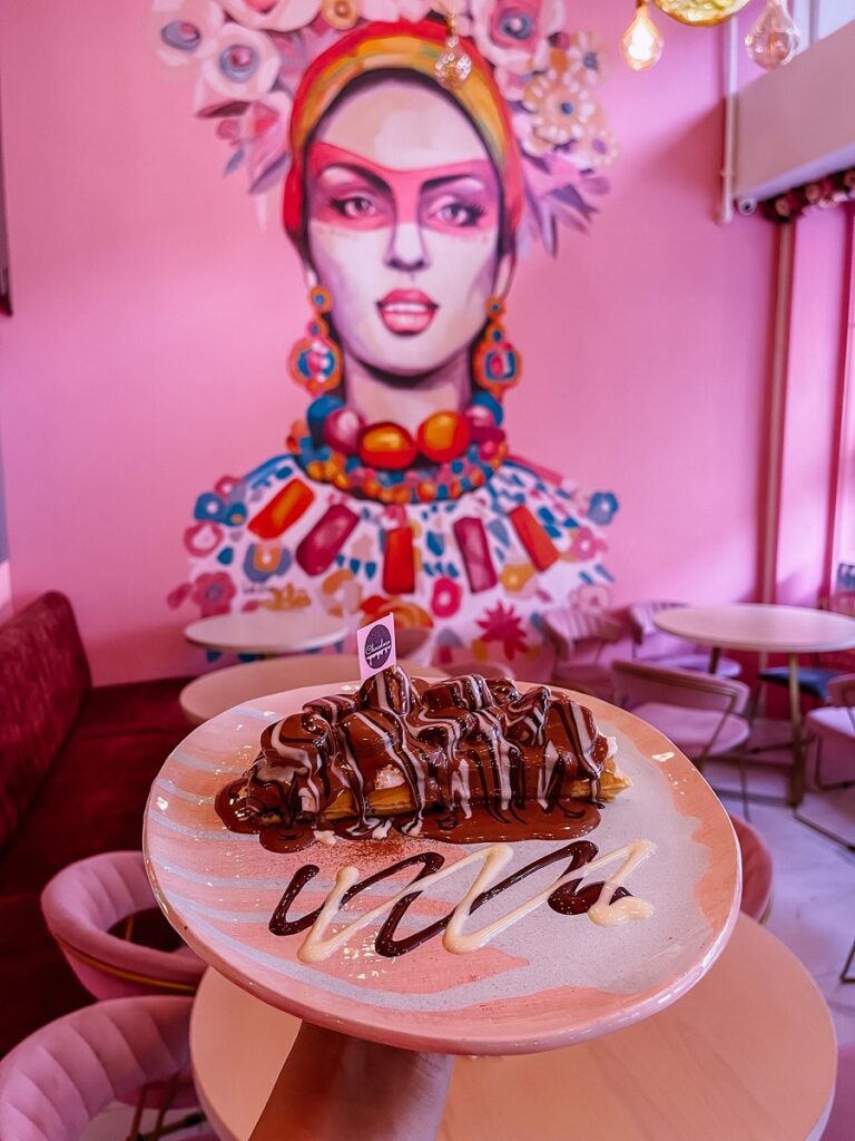 prajitura cu ciocolata pe o farfurie in prim plan, iar in fundal un perete roz cu o pictura murala mare ce infatiseaza o femeie, la cofetaria Chocoloco, unde să ieși cu prietenele de 1 martie