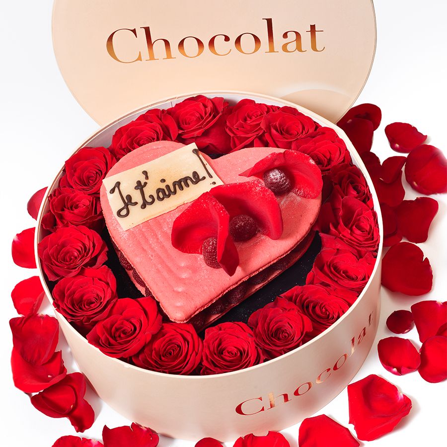 cutie de Valentines Day cu tort de bezea roz, in forma de inima, asezat printre trandafiri
