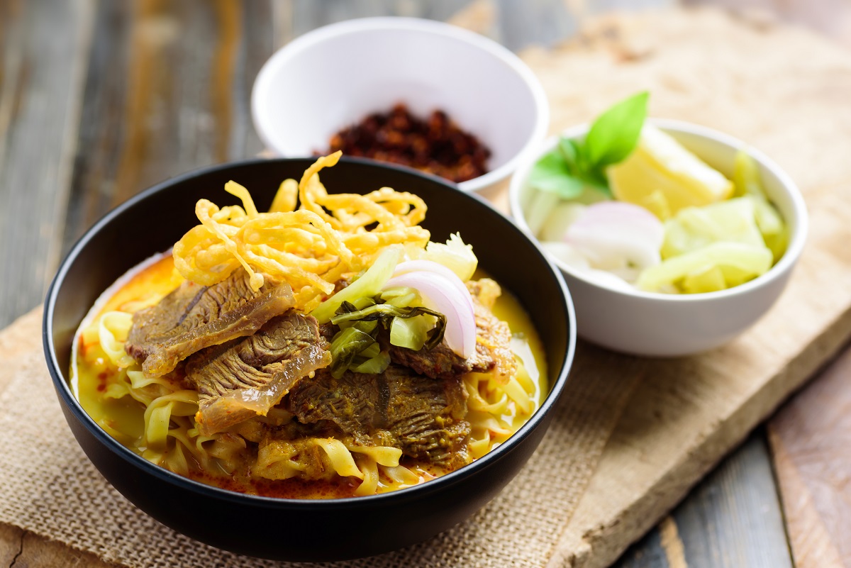 Northern Thai food (Khao Soi), Spicy curry noodles soup with beef in a bowl eating with crispy deep-fried egg noodles, pickled mustard, shallots, lime and ground chillies fried in oil