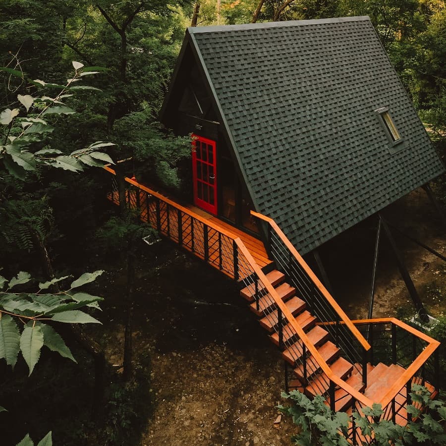 Cabana neagra de tip A frame, cu scara din lemn rosiatic, la Porumbacu Treehouse, un d in destinații romantice din România
