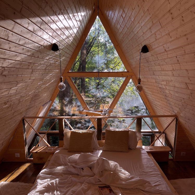 pat asezat in dreptul unei ferestre prin care se vad copaci, intr-o cabana de tip A frame