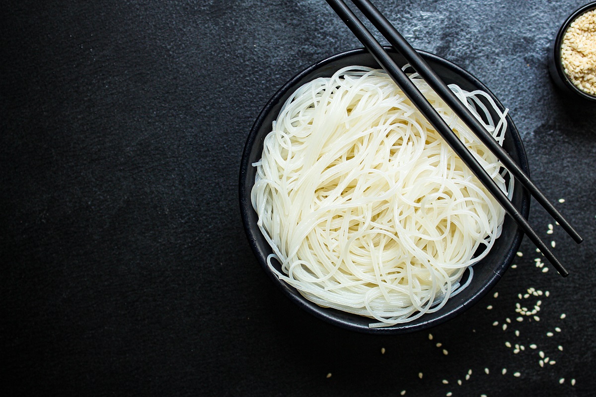 bol negru cu taitei asiatici, si doua bete negre asezate deasupra, fotografiat de sus, pe fundal negru - tipuri de noodles